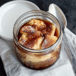 Single-serve French toast in a mason jar topped with maple syrup, placed on a white kitchen counter in natural light