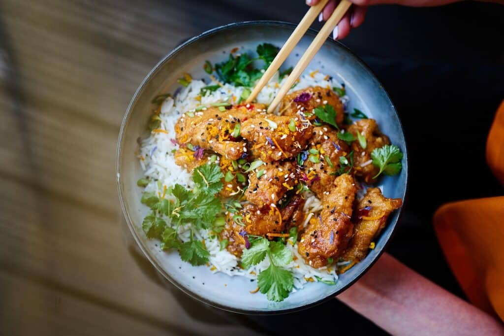 A woman's hand holding a bowl of chicken and rice