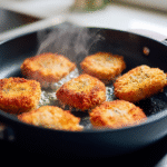 six keto nuggets frying in non-stick skillet, one flipped with spatula