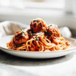 Flat lay of a bowl of cooked spaghetti and meatballs beside ingredient portions on a marble counter, clean measuring spoons and prep bowls visible, ready for recipe card, white modern kitchen, bright light, 3:2